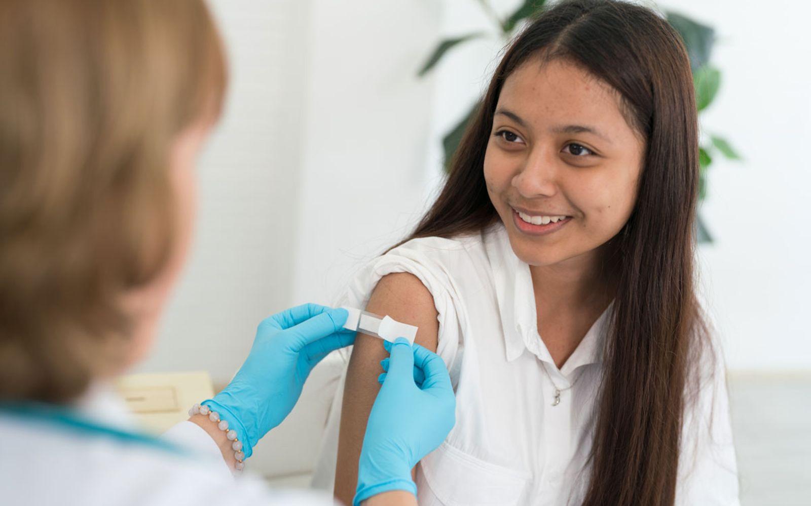 HPV-Impfung: Ärztin klebt einer Teenagerin nach der Impfung ein Pflaster auf den Arm.